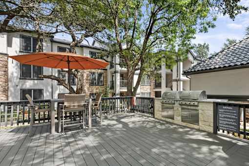A wooden deck with a table and chairs and a red umbrella.