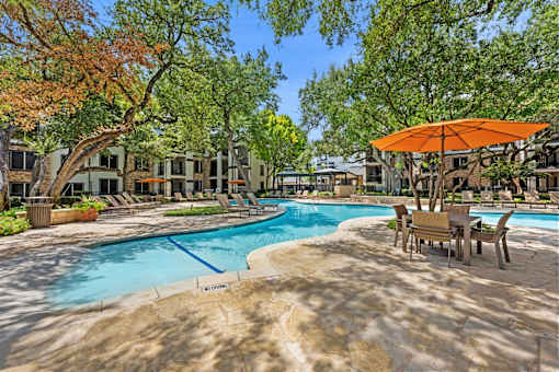 A pool surrounded by trees and chairs with an orange umbrella.