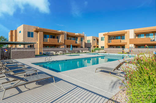 A swimming pool is surrounded by sun loungers in front of a building.