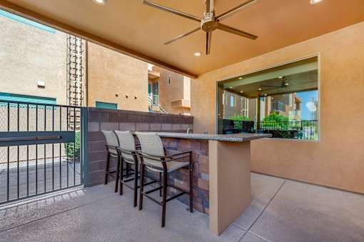 A patio with a bar and chairs under a ceiling fan.
