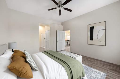 A bedroom with a bed, a ceiling fan, and a painting on the wall.