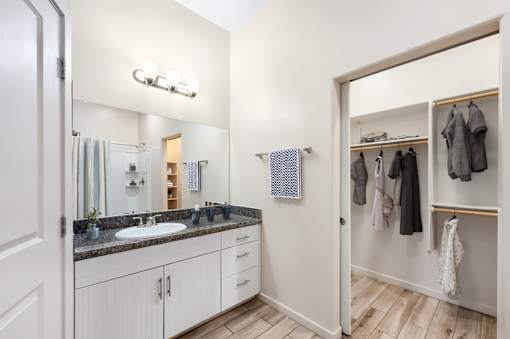 A bathroom with a sink, mirror, and a closet with clothes.