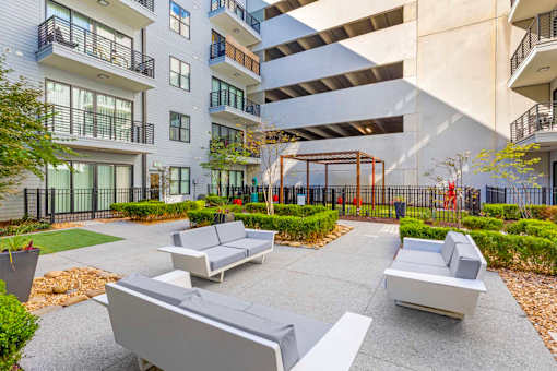 A modern outdoor seating area with grey couches and a black fence.