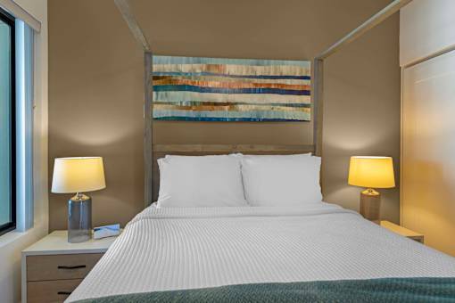 A bedroom with a large bed, two lamps, and a painting on the wall.