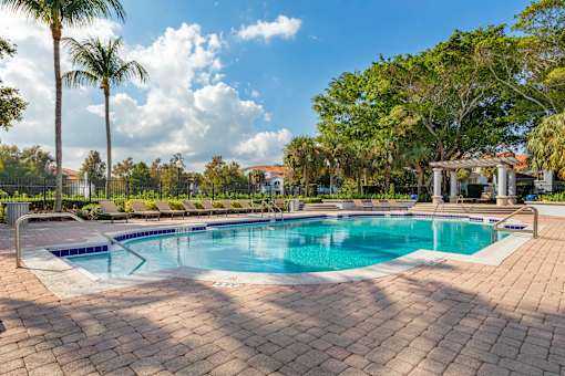 A large outdoor swimming pool surrounded by a brick patio and palm trees.