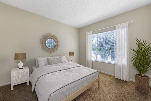 A bedroom with a large bed, a round mirror, and a potted plant.