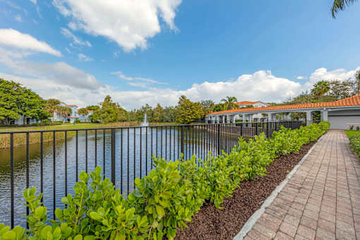 A walkway overlooking the water and a fountain with a metal railing and green landscape on the side.