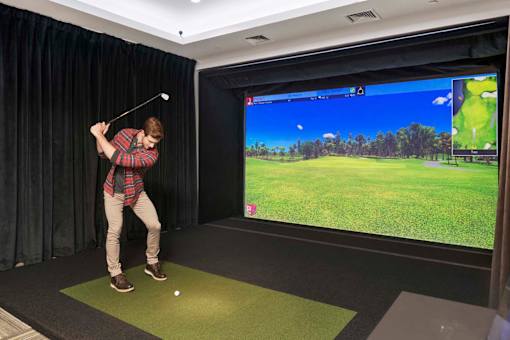 A man is playing golf in a room with a large screen showing a golf course.
