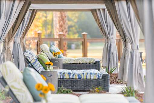 A patio with grey curtains and a couch with a yellow flower on it.