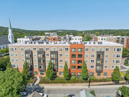 an aerial view of an apartment building with a church in the background at The Merc, Waltham, 02453
