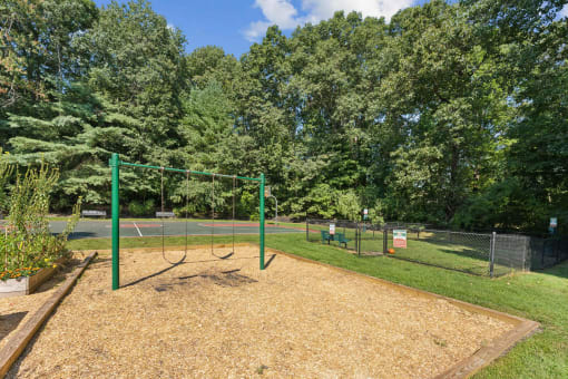 a swing set in a park next to a tennis court at Residences at Westborough Station, Westborough, MA, 01581