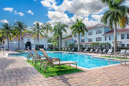 A pool surrounded by palm trees and lounge chairs.