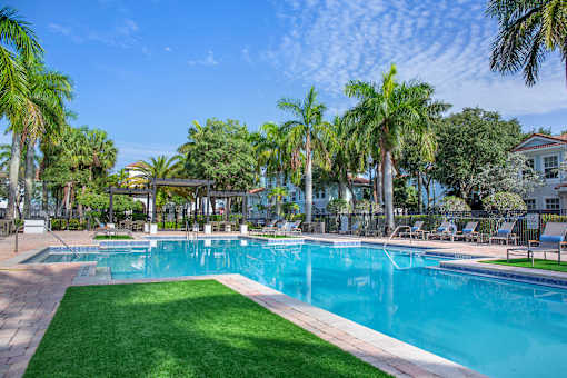 A large swimming pool surrounded by palm trees and lounge chairs at Floresta apartments in Jupiter, FL