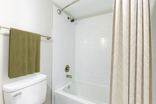 A white toilet with a green towel hangs over a white bathtub.