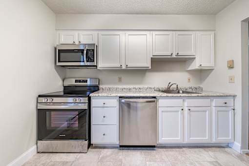 an empty kitchen with white cabinets and stainless steel appliances