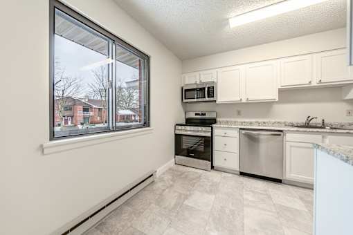 an empty kitchen with a large window and white cabinets