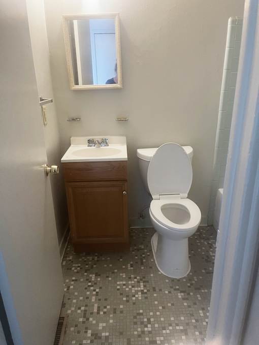 The bathroom in a 1 bedroom unit with white and chrome fixtures.