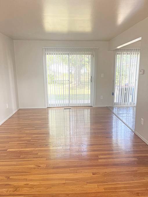 A bright living room with a sliding glass door that leads to the outdoors. The floors are shining wood and the walls are light colored.