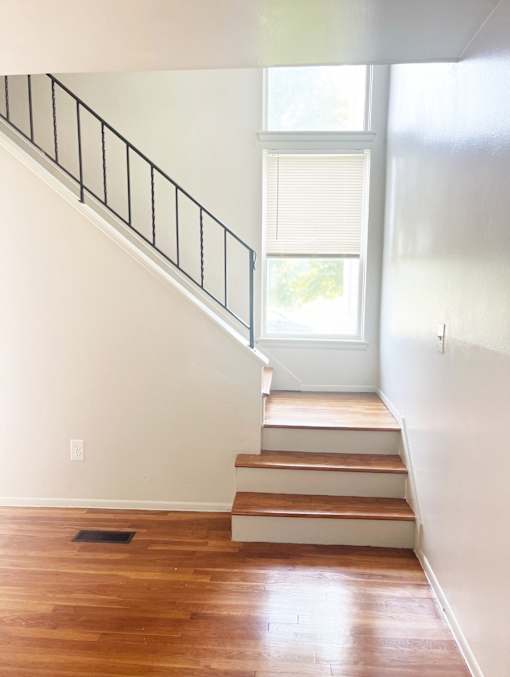 A photo of a bright staircase with a window and a black railing.
