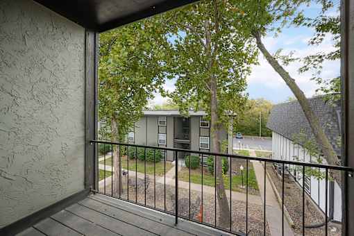 A balcony with a black railing and a view of a tree and a building.