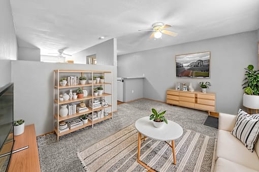 A living room with a white ceiling fan, a white coffee table, a wooden shelf with plants, and a striped rug on the floor.