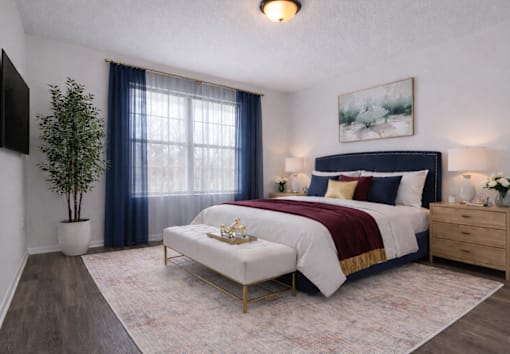 An apartment master bedroom with a large bed, a small table, and a potted plant.