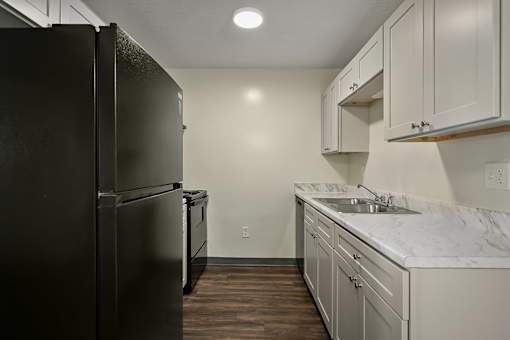 A kitchen with a black refrigerator and white cabinets.