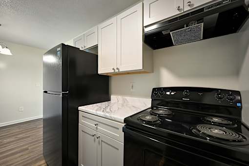 A black refrigerator and stove in a kitchen with white cabinets.
