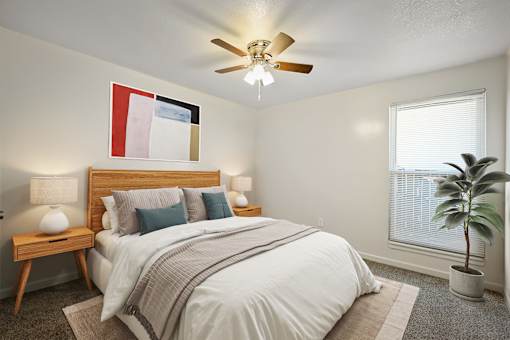A bedroom with a bed, a ceiling fan, and a potted plant.
