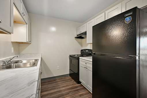 A black fridge in a kitchen with white cabinets and a stainless steel sink.