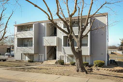 A tree in front of a two-story apartment building.