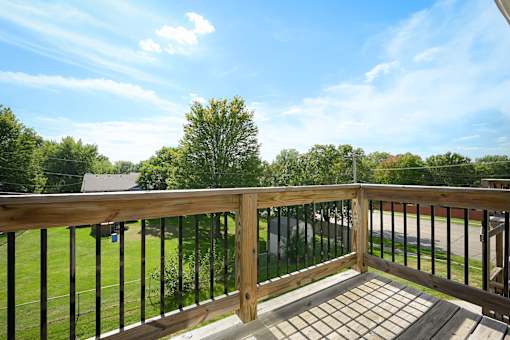 A wooden deck with a black railing and a view of a green lawn and trees.