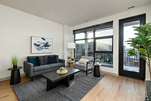 A modern living room with a grey couch, a coffee table, and a large window.at Raymond Block, Edmonton, AB