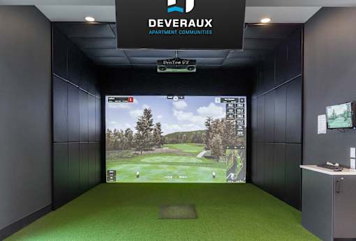 A room with a green carpet and a screen showing a golf course.