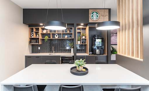 A modern dining area with a white table and chairs, a potted plant on the table, and a Starbucks sign on the wall at Skyway Apartments, Alberta, T3B 5V6