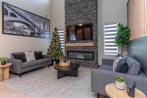 A living room with a grey couch, a coffee table, a fireplace, and a Christmas tree.at Vibe Apartments at Arbour Lake, Calgary Alberta  