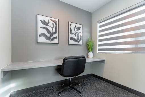 A black chair is in front of a desk with two framed pictures on the wall.at Vibe Apartments at Arbour Lake, Calgary  