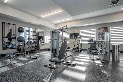 A well-equipped gym with various exercise machines and a person working out.at Vibe Apartments at Arbour Lake, Calgary  