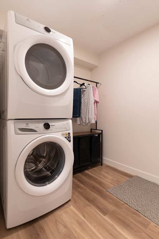 A white front loading washing machine is stacked on top of another one in a laundry room.at Vibe Apartments at Arbour Lake, Calgary, AB  
