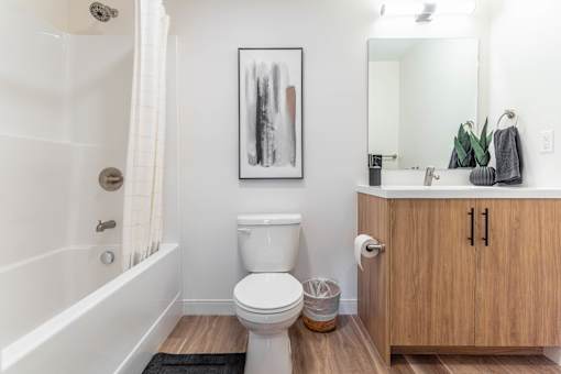 A white toilet sits in a bathroom next to a wooden cabinet.at Vibe Apartments at Arbour Lake, Calgary, AB T3G 4J2  