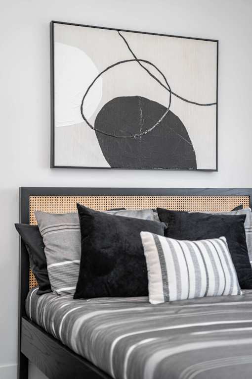 A bed with striped bedding and pillows in front of a black and white abstract painting.at Vibe Apartments at Arbour Lake, Calgary, AB  