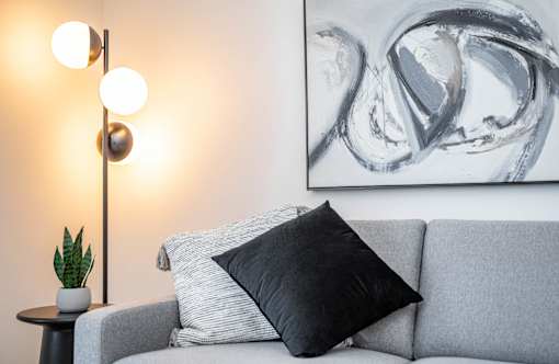 A grey couch with a black pillow and a silver floor lamp.at Vibe Apartments at Arbour Lake, Alberta  