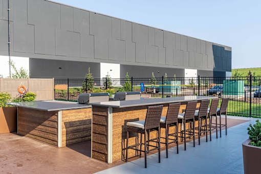 A modern outdoor bar area with wooden stools and a counter. at G17 Apartments at Tamarack, Edmonton, AB