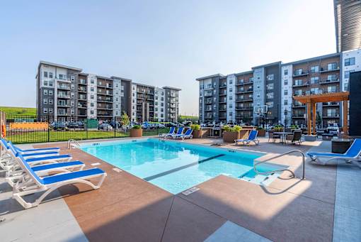 A swimming pool surrounded by sun loungers and chairs in front of apartment buildings. at G17 Apartments at Tamarack, Edmonton, AB