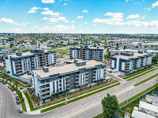 A large apartment complex is situated on a street corner with a road and cars in the foreground.