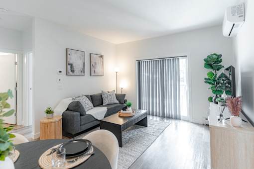A modern living room with a grey sofa, a black coffee table, and a large window with blinds.