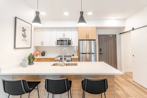 A modern kitchen with a white countertop and black chairs.