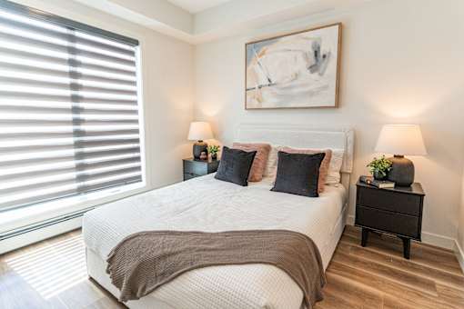 A bedroom with a large bed, two lamps, and a painting on the wall.
