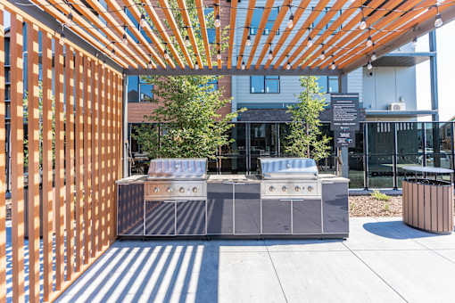 A modern outdoor kitchen with a grill and a wooden pergola.