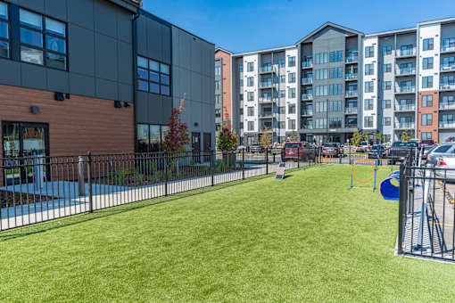A playground with a slide and swings is surrounded by a fence and a grassy area in front of a building.